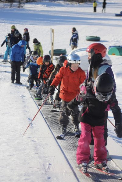 Young beginner skiers going up the ski escalator